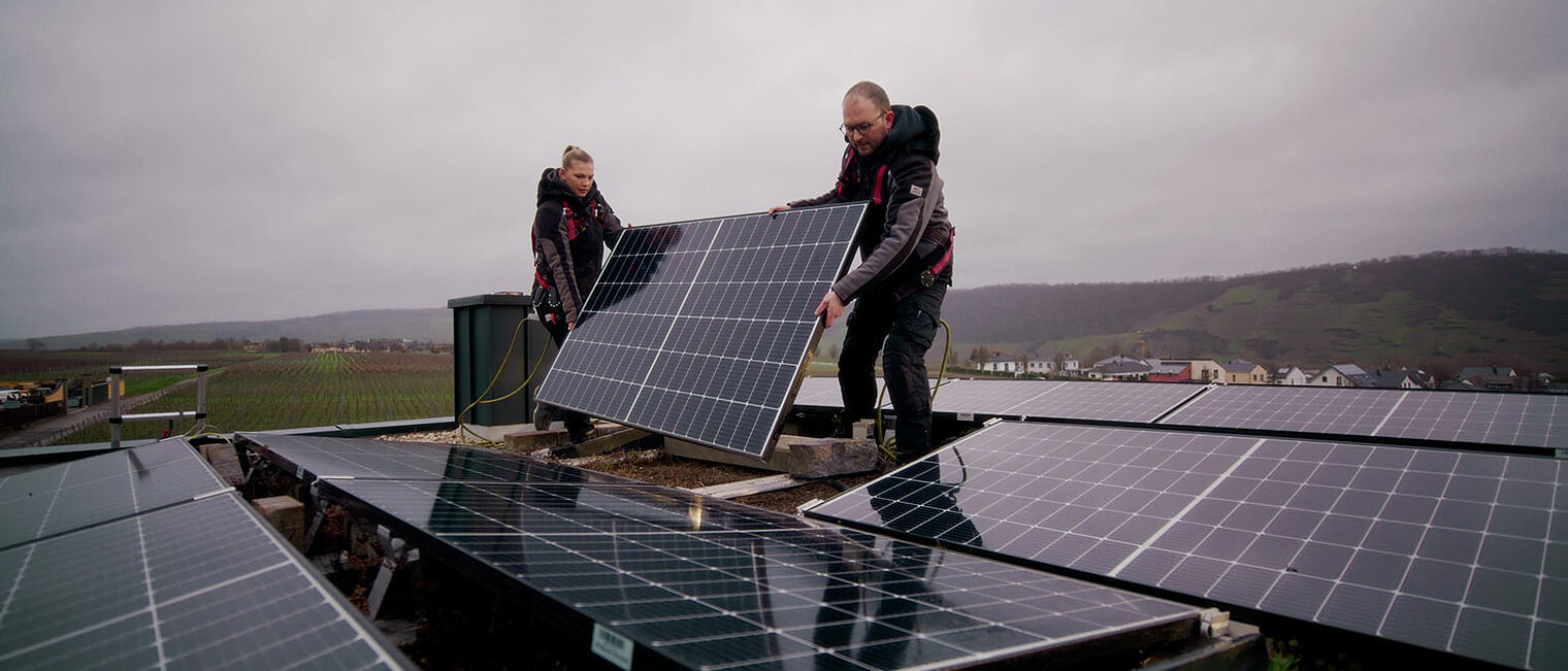 Zwei Handwerker installieren eine Photovoltaikanlage auf einem Dach.